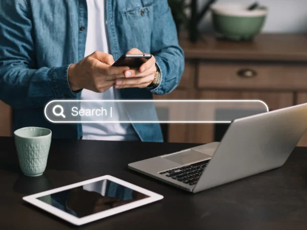 Imagem que ilustra SEO para Google Discover: O que Difere da Busca Tradicional? Um homem usando smartphone e laptop em uma mesa.