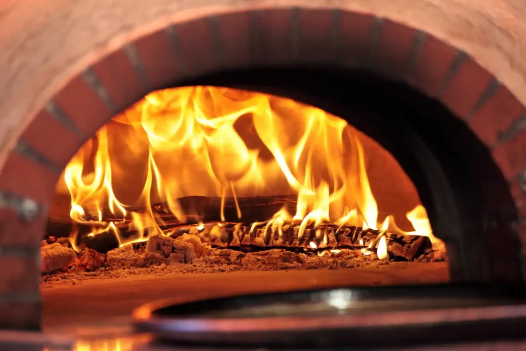 Imagem de um forno de lastro aceso com fogo dentro, mostrando diferenças entre forno de lastro e forno turbo para escolha em negócios de alimentação.