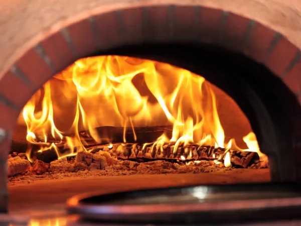 Imagem de um forno de lastro aceso com fogo dentro, mostrando diferenças entre forno de lastro e forno turbo para escolha em negócios de alimentação.