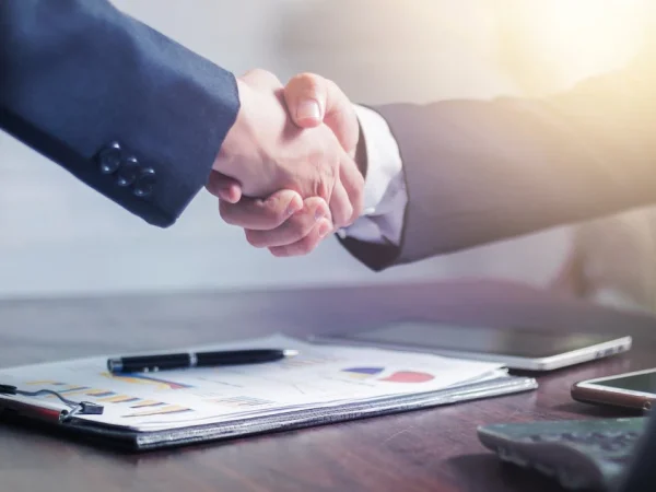 Imagem de dois empresários dando um aperto de mãos após negociação, representando a prática do Orçamento Base Zero (OBZ) na gestão financeira.