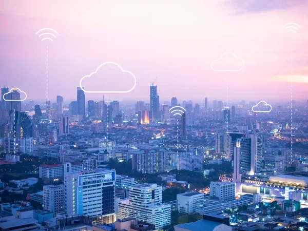 Vista panorâmica de uma cidade brasileira ao entardecer com arranha-céus e camadas de ícones de nuvem e sinal de Wi‑Fi, simbolizando Cidades Inteligentes: como a tecnologia está transformando a vida urbana no Brasil.