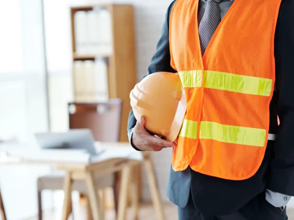 Trabalhador em ambiente de fábrica usando capacete de segurança e colete laranja refletivo, postura voltada para prevenção e boas práticas de Segurança do Trabalho na Era Digital.